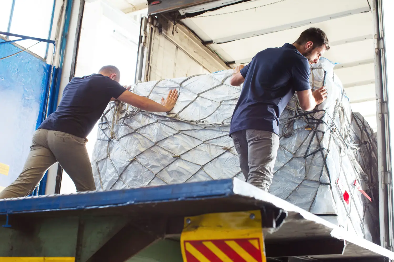 Zwei Männer verladen große verpackte Fracht in einen LKW im Rahmen eines Beiladungstransports in Hamburg