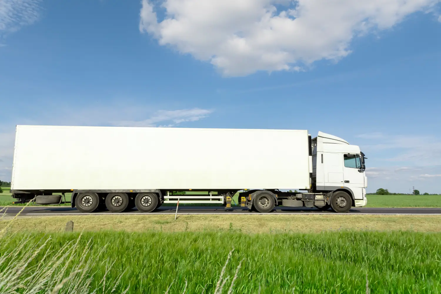 eißer LKW mit großem Auflieger fährt über Landstraße bei blauem Himmel im Rahmen eines Schwertransports ab Hamburg